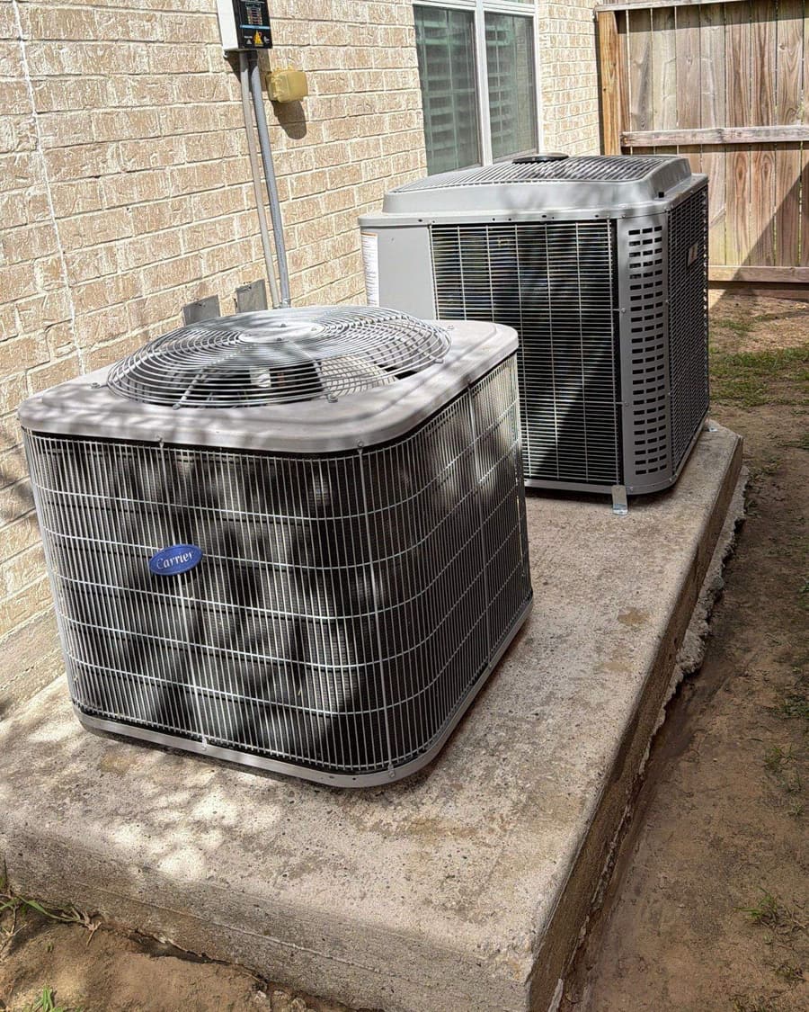 Two outdoor condensers on a pad beside a brick home