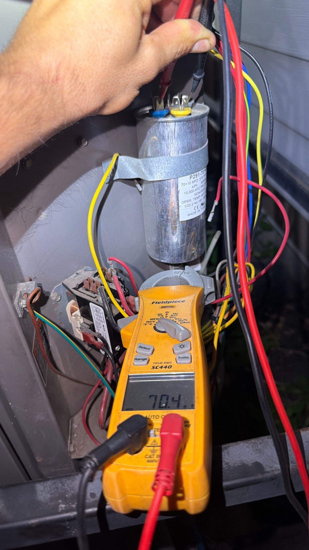 ColdSolutions technician meter-testing an AC capacitor during a repair call