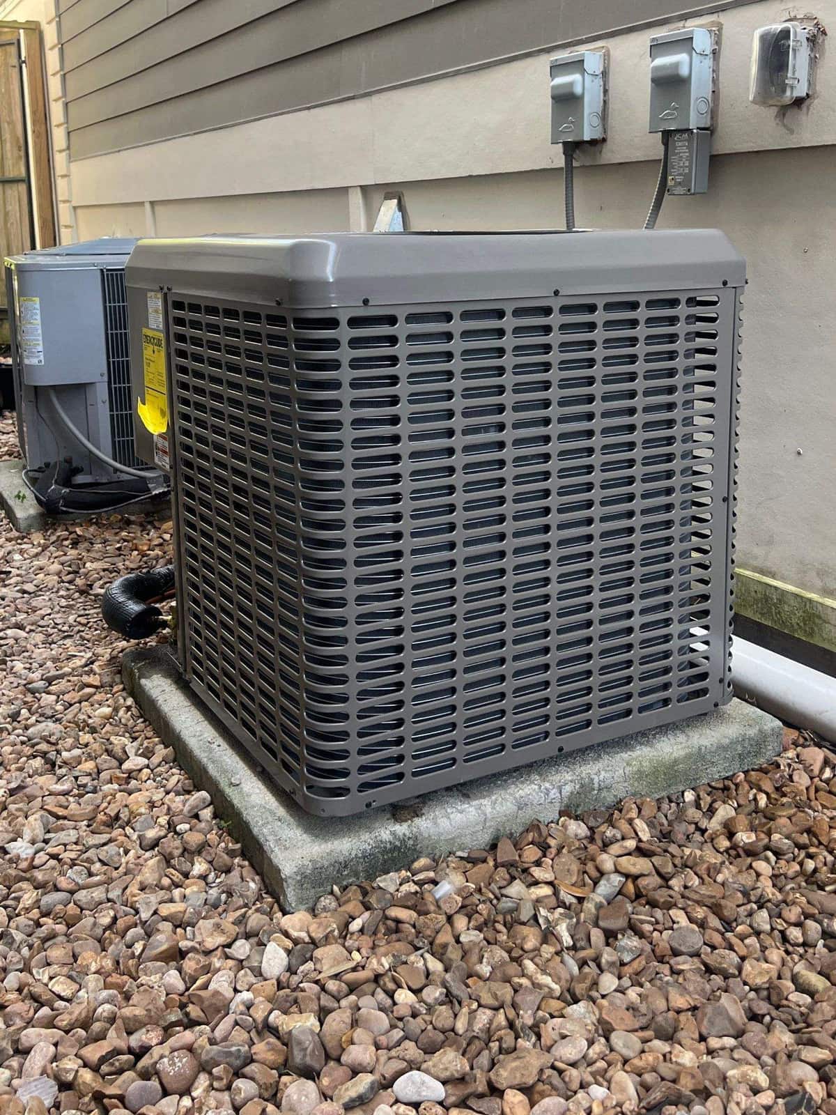 New condenser set level on a pad in a gravel bed beside gray siding