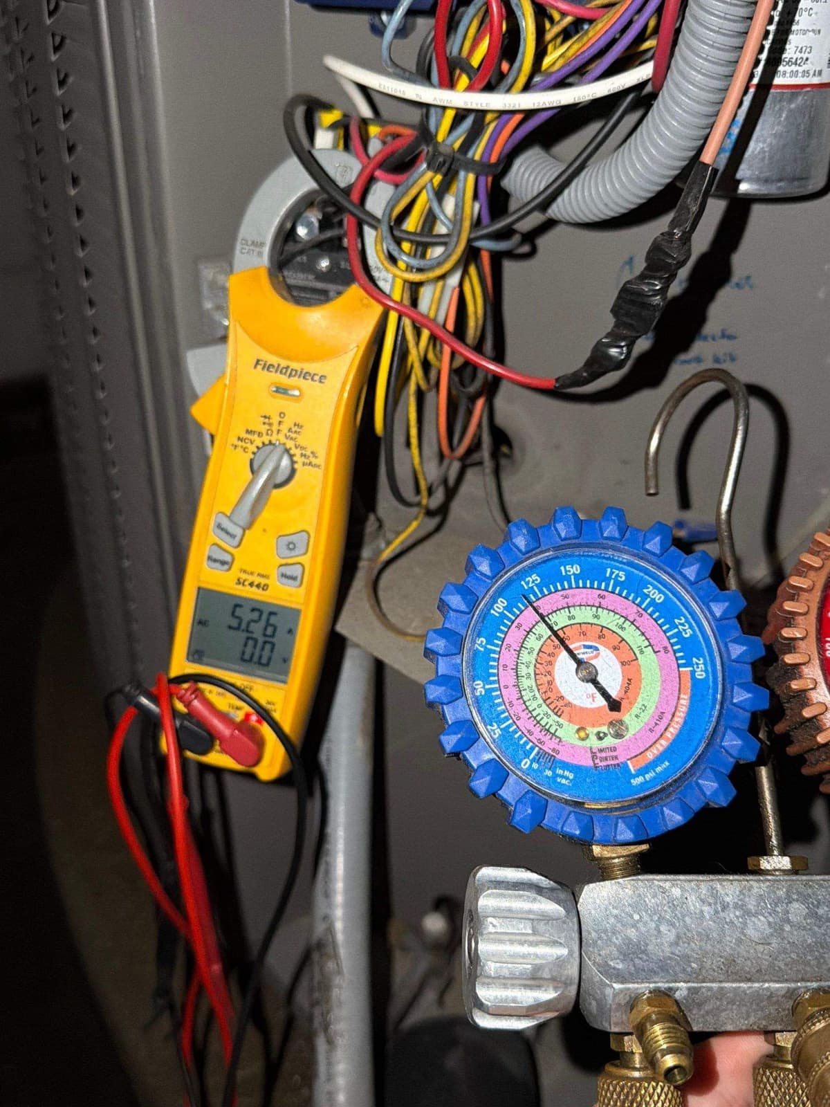 Technician reading refrigerant gauges and a clamp meter on an outdoor AC unit
