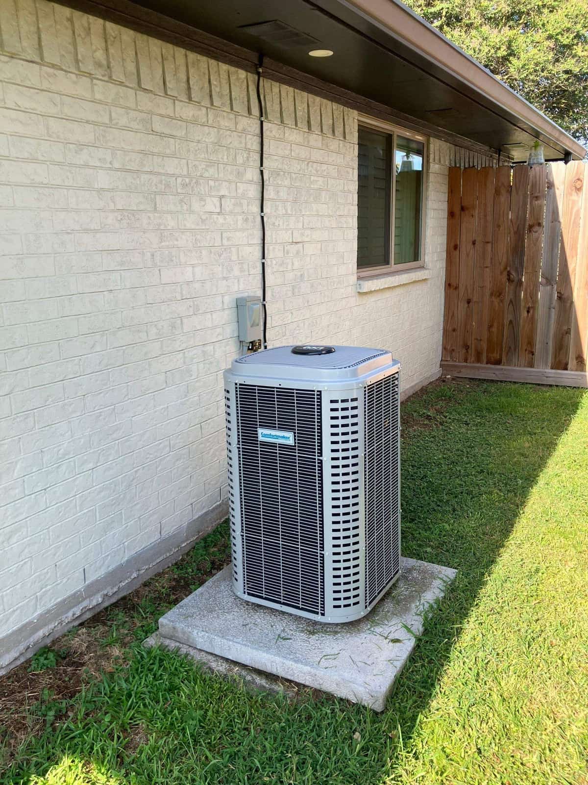Outdoor condenser on a pad beside a light brick home and lawn