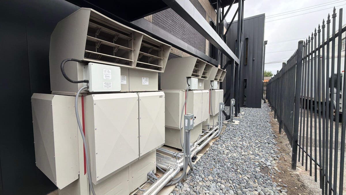 Row of commercial condensing units along a building behind a fence