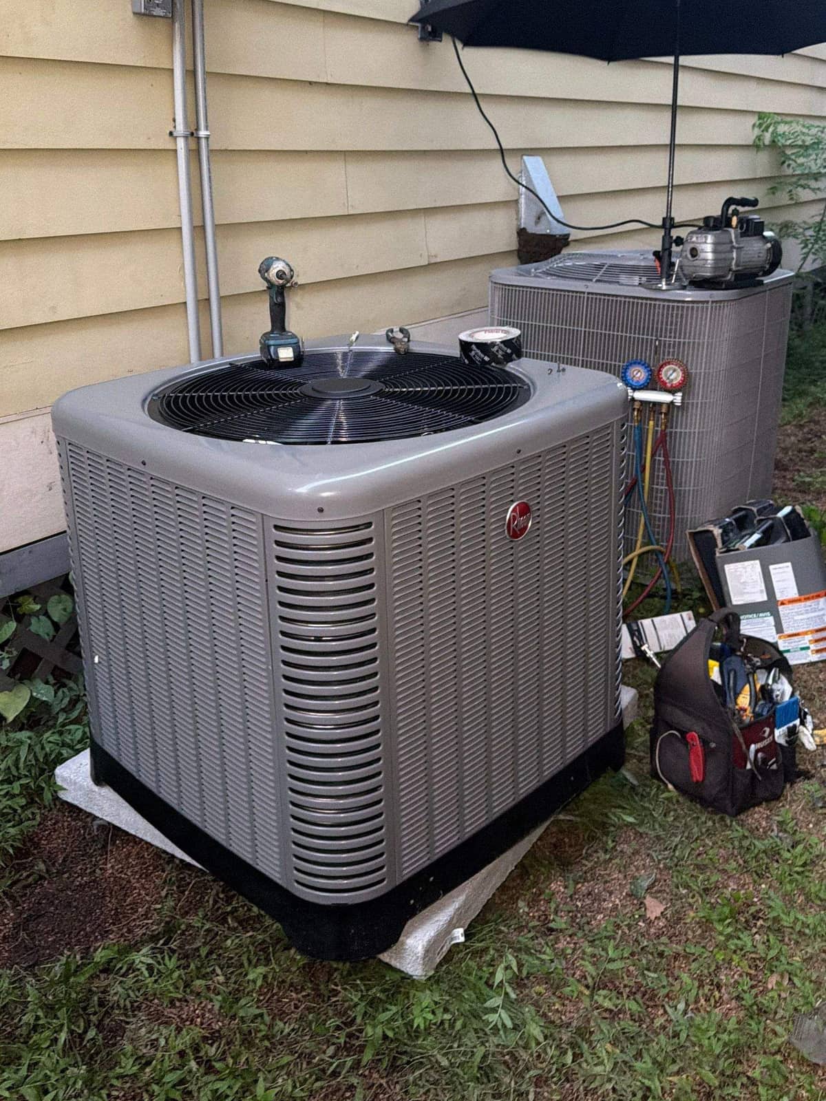 New condenser on a pad beside siding, with a patio umbrella behind it