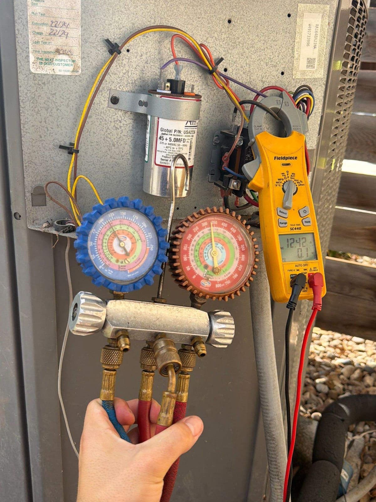 Technician holding refrigerant gauges against an outdoor unit