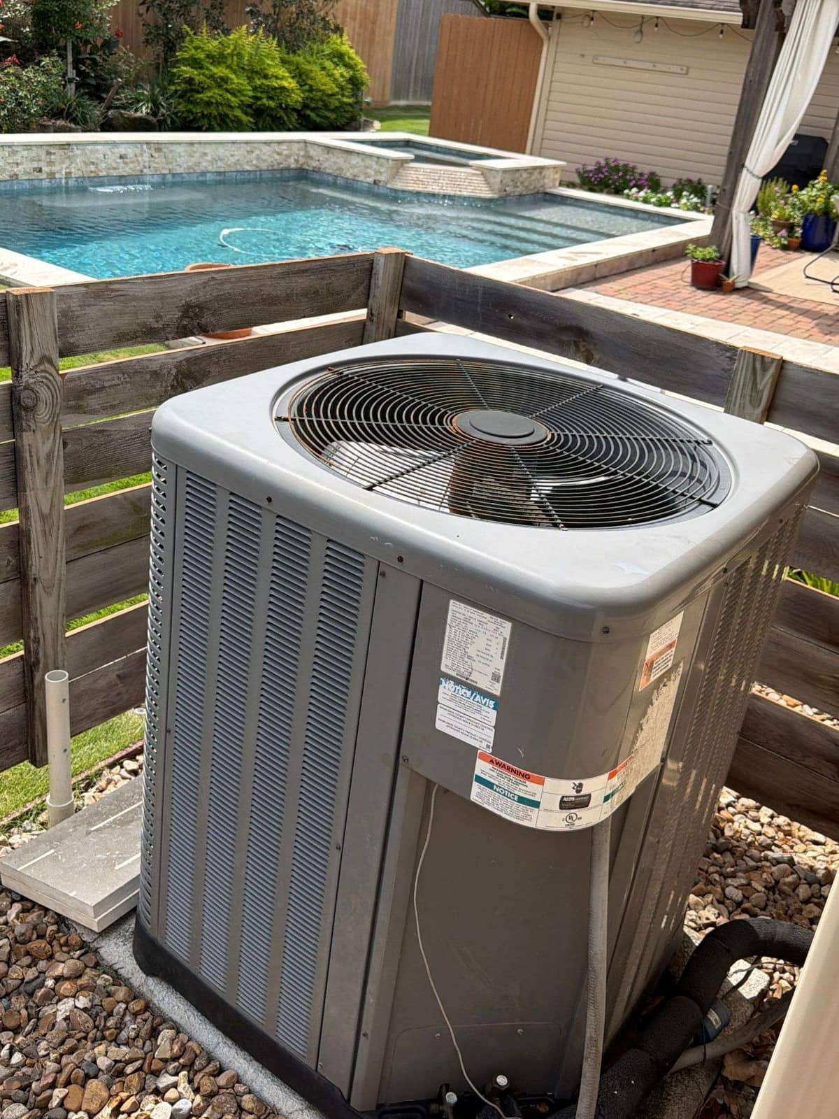 Outdoor condenser inside a wood fence beside a backyard pool