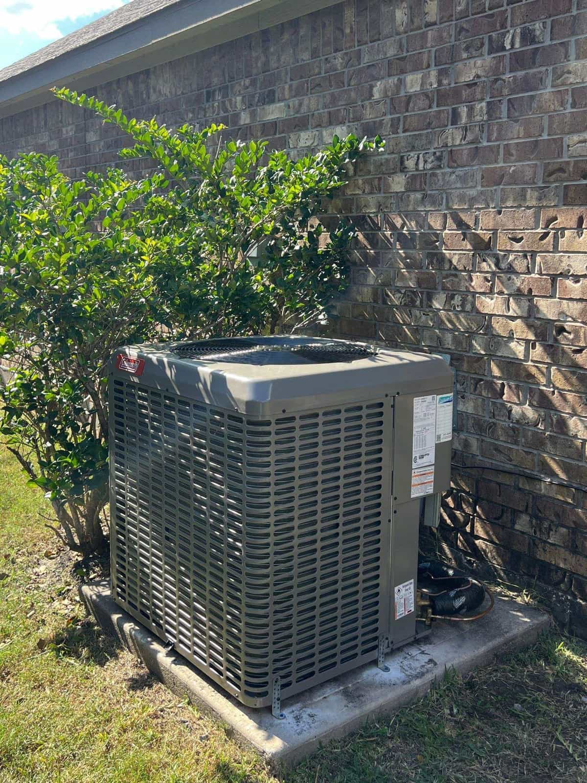 New condenser beside a brick home with shrubs