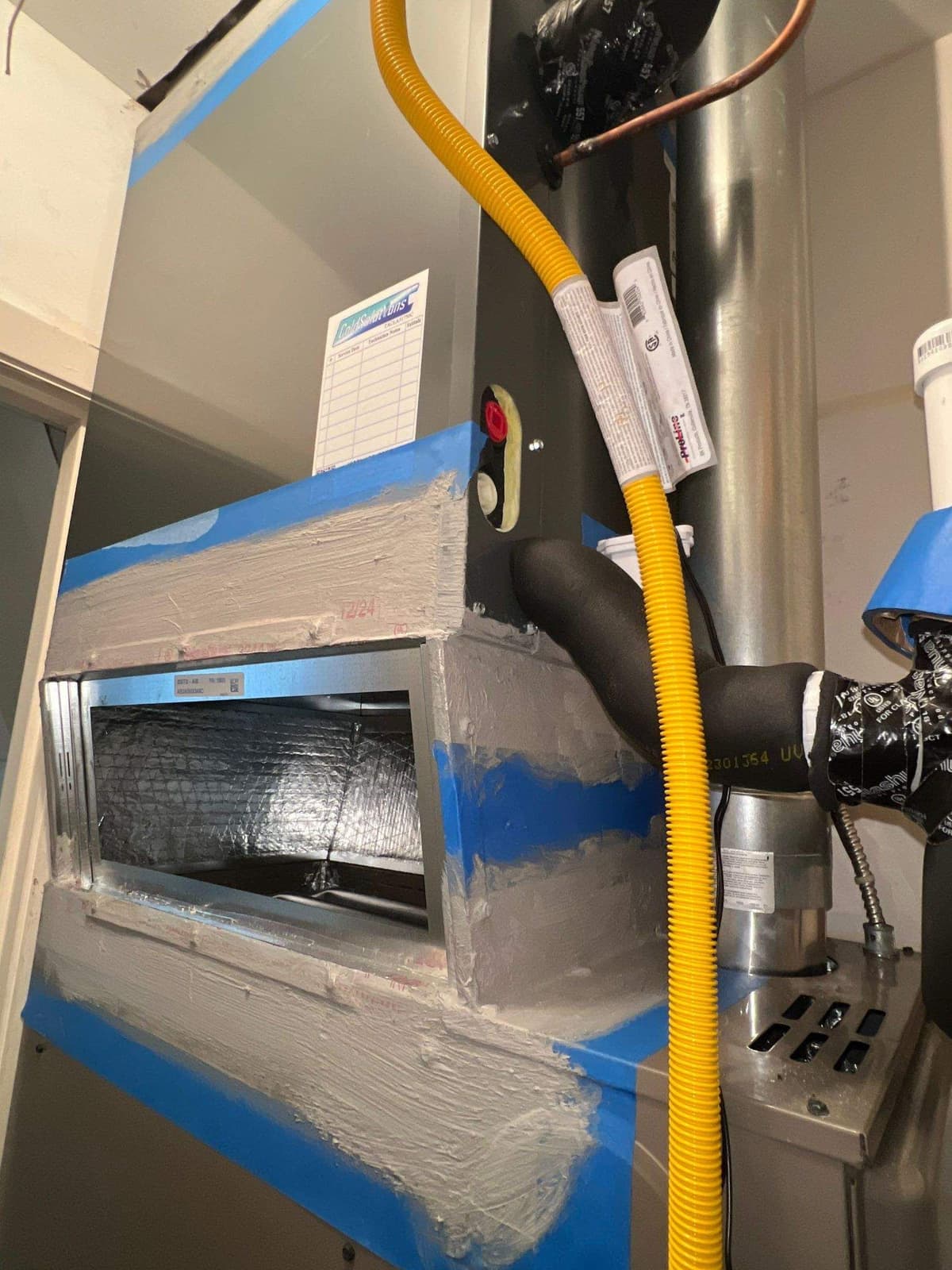 Furnace in a closet with a yellow gas line and fresh foil tape on the plenum