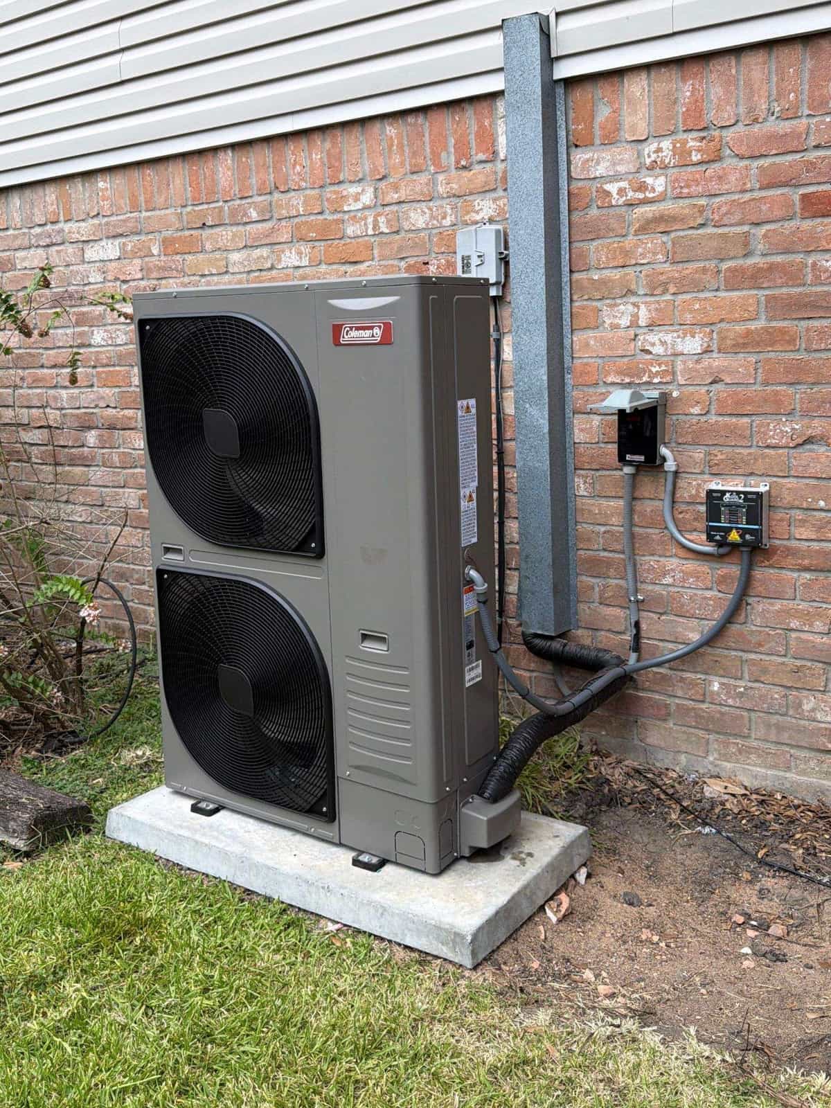 New two-fan heat pump set on a fresh pad beside a brick home