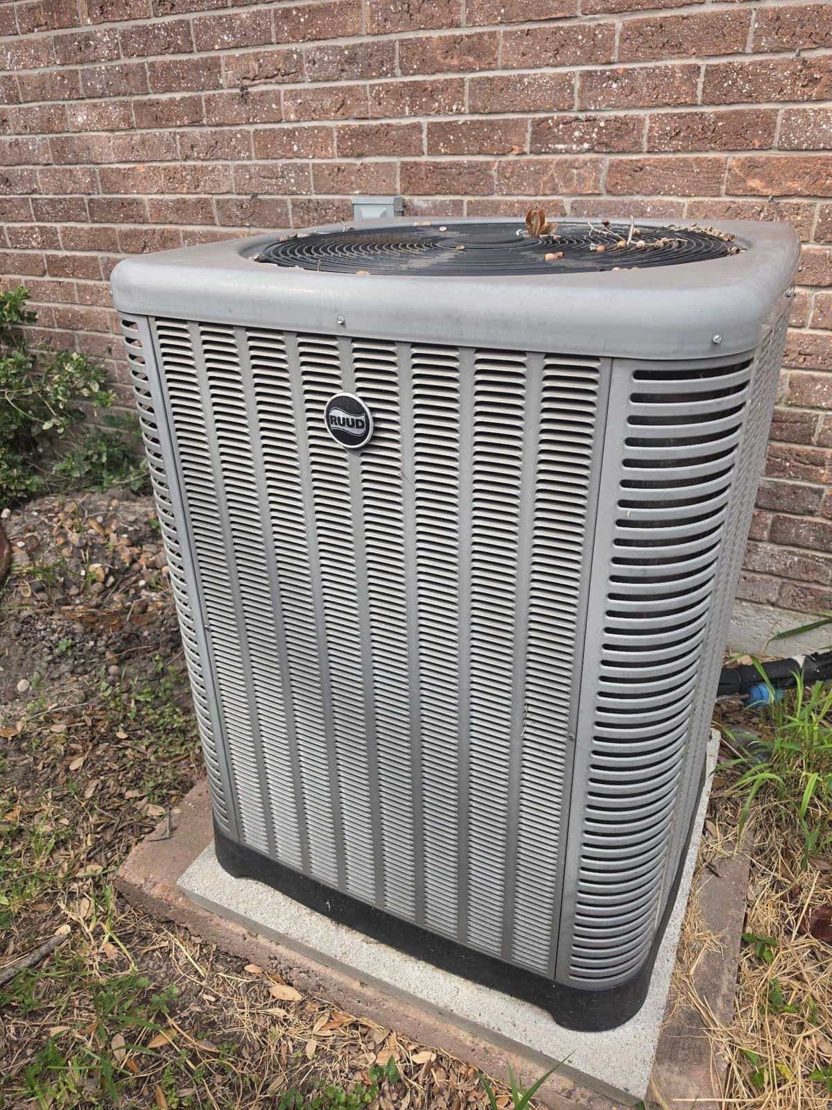 New Rheem condenser on a pad beside a brick wall