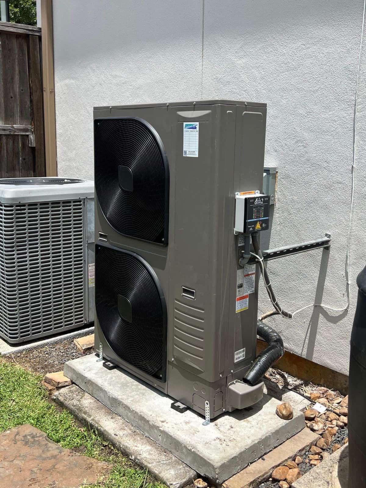 Two-fan heat pump beside an older condenser on a new pad