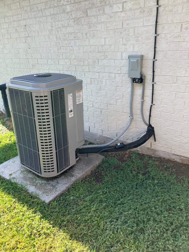 Outdoor condenser on a pad beside a brick wall and lawn