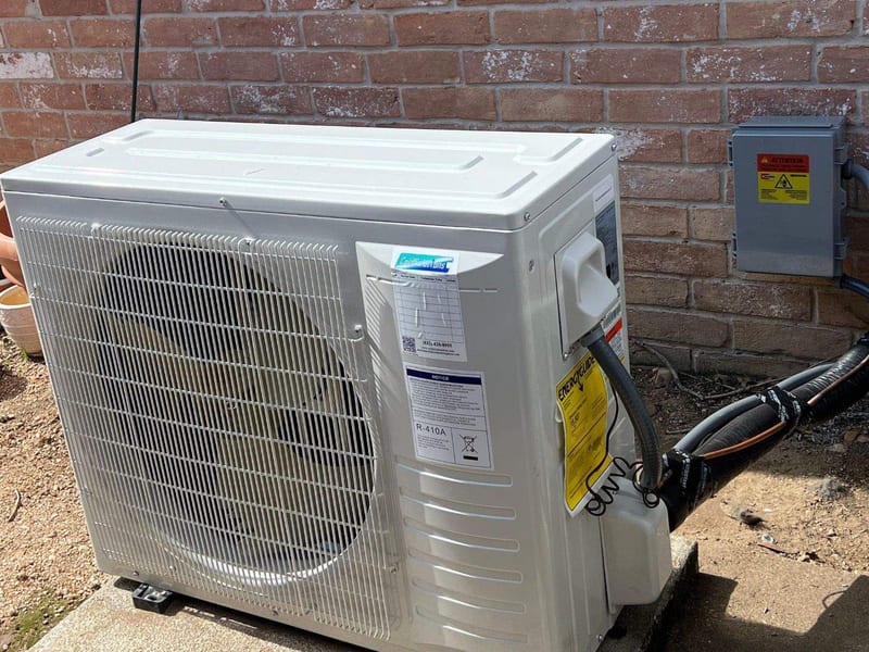 Ductless outdoor unit on a pad beside a brick wall